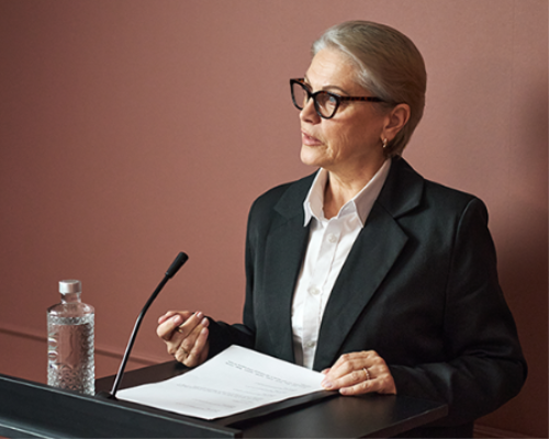 Woman with glasses and blazer speaking at a podium