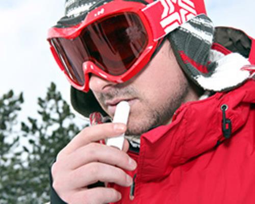 Man in red ski googles and heavy coat applying chapstick to his lips