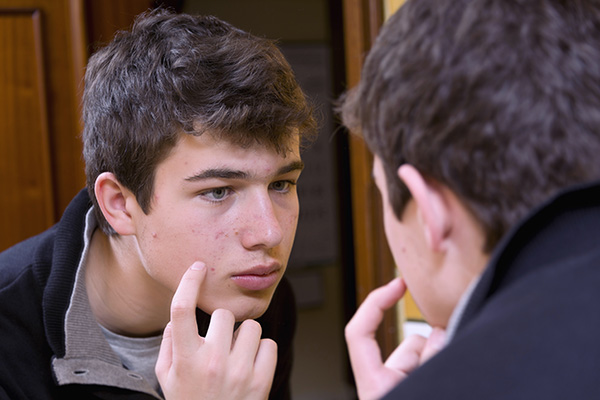Dark haired male teen looking closer at acne in mirror