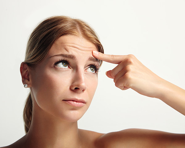 Young female with a slightly concerned expression looking up towards her finger lifting her brow line up