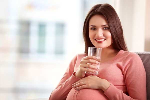 seated pregnant young women with class of water and hand resting on her stomach