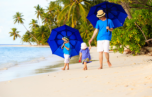 Father and two children walking on a beach with big blue sun umbrellas 