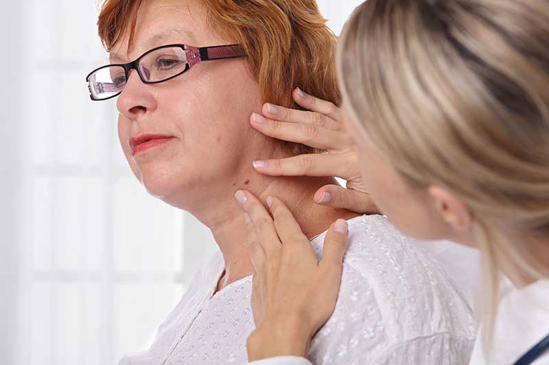 Female patient have a neck mole checked by a female medical professional