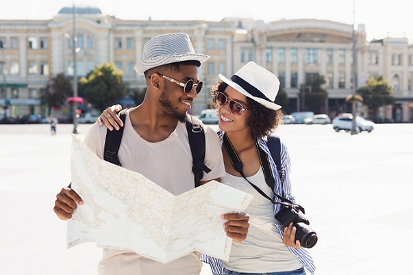 Darker skinned man and woman dressed in white sun hats with holding a map and camera on a sunny afternoon