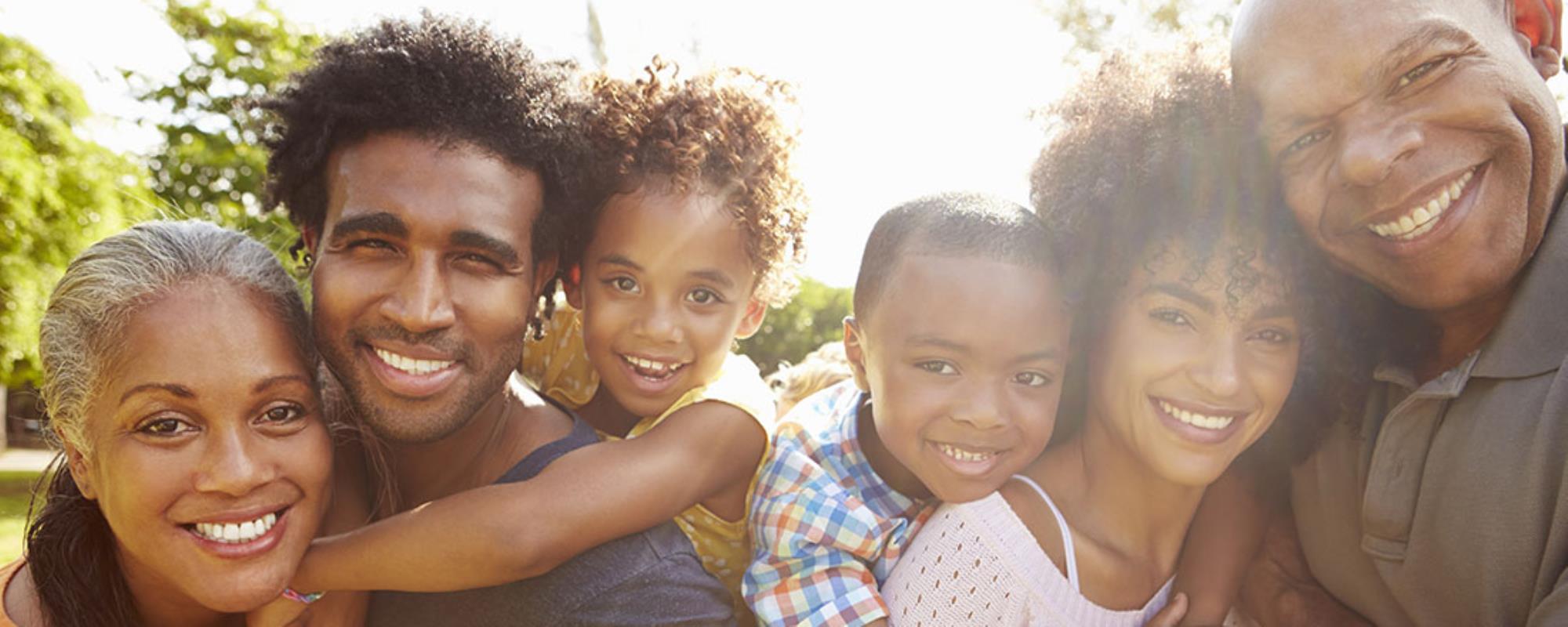 Dark skinned family ranging in ages smiling for a photo on a sunny day