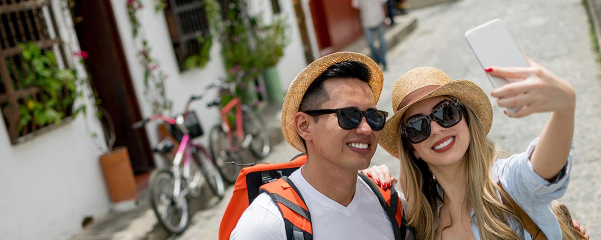 Couple on vacation wearing sunglasses and straw hats taking a selfie on a eccentric street