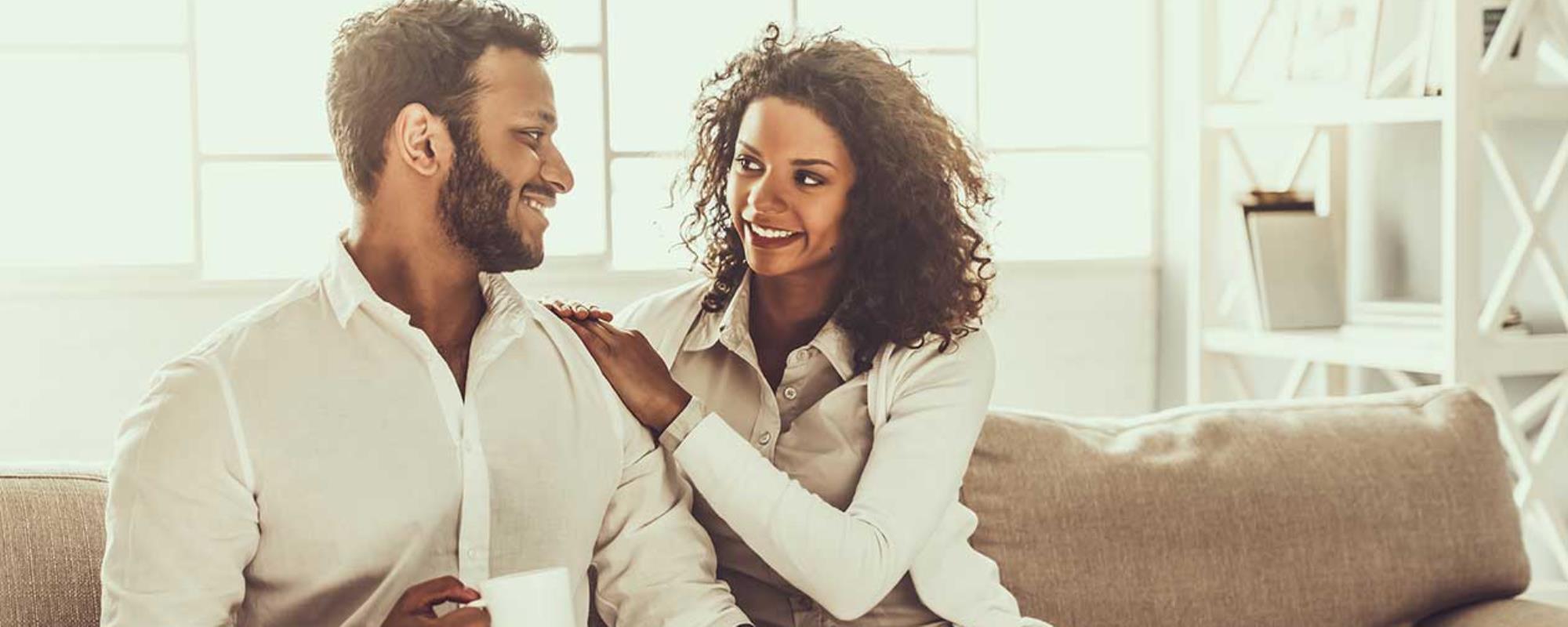 couple dressed in white smiling at each other while enjoying coffee