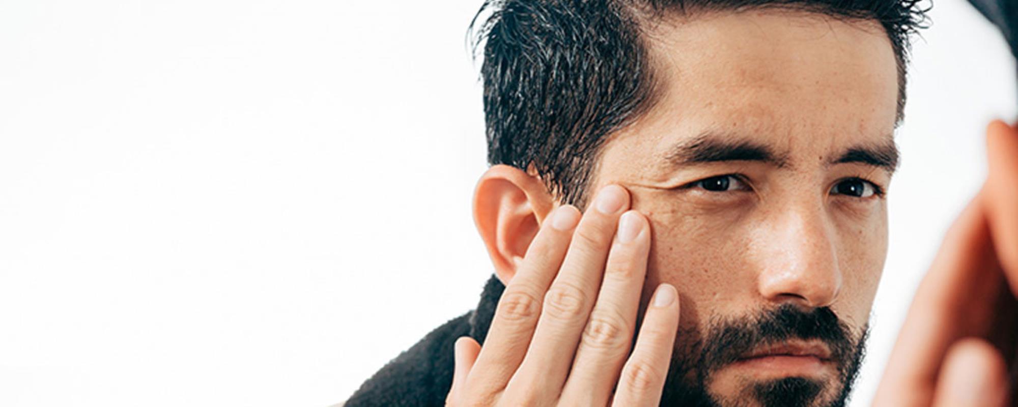Middle aged man stretching cheek and eye skin looking at wrinkles in mirror