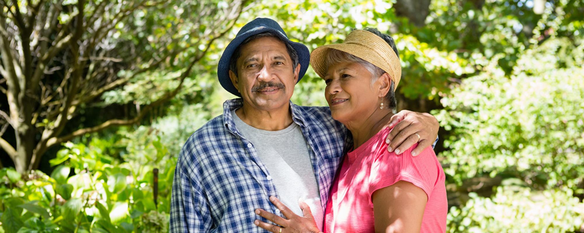 50+ couple in relaxed summer attire having their photo taken against a lush garden background