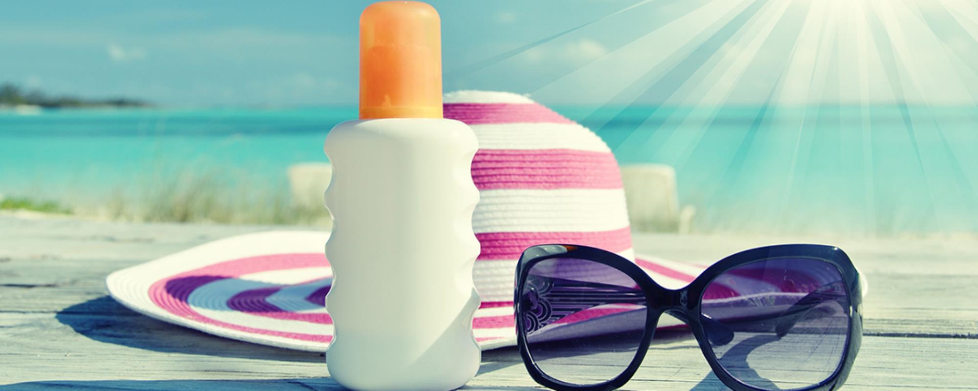 Sunscreen, pinked na white striped sunhat and cat eye shaped sunglasses set in a summer beach setting