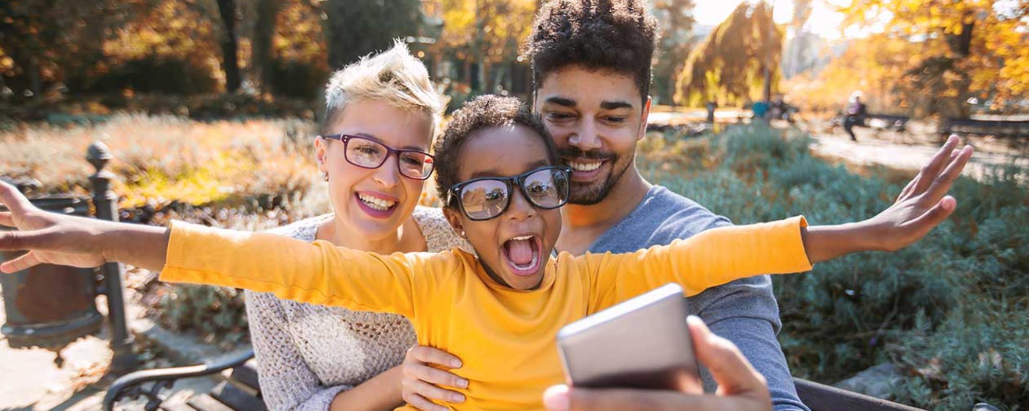 Diverse family taking a group selfie on a park bench in autumn