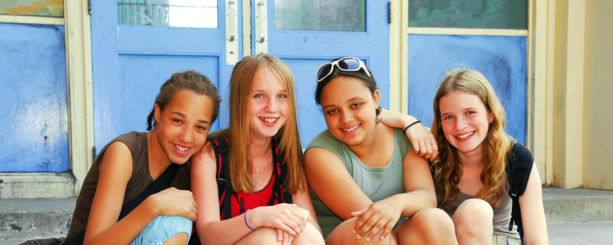 Group of diverse teen girls posing in front of school doors