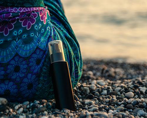 Woman sitting on beach with sunscreen product next to her hip
